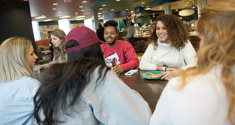 Group of students talking and eating at a table in the Watterson dining center.